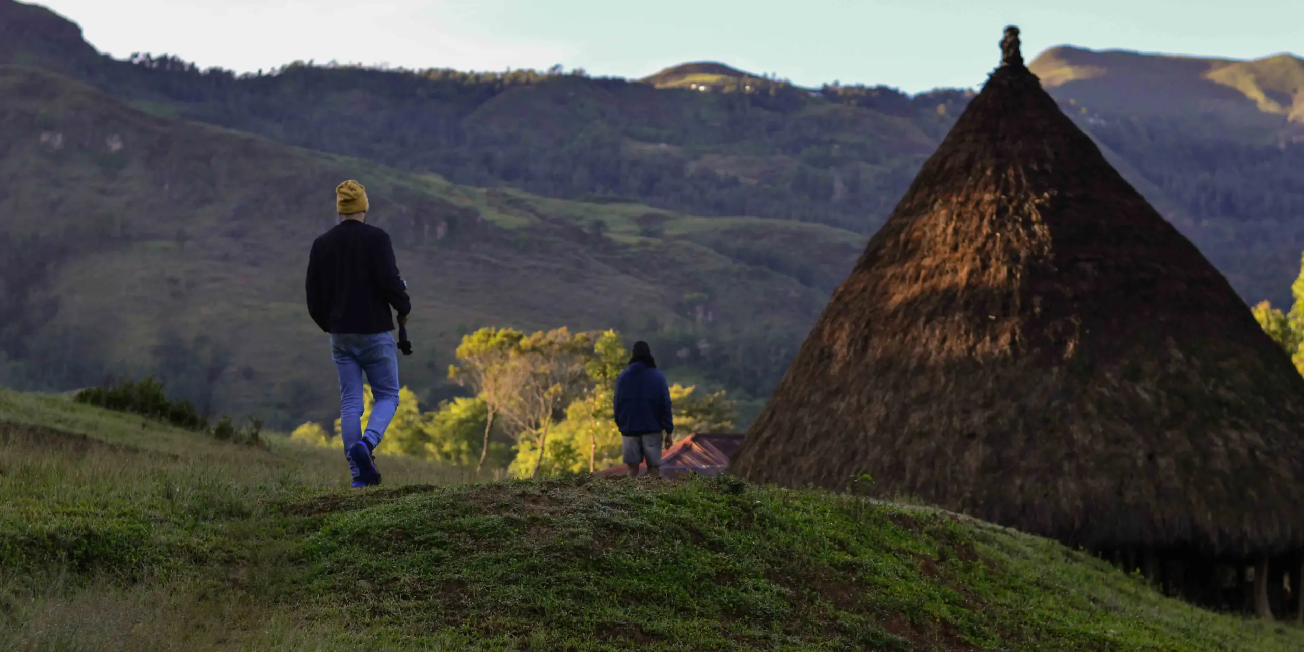 Visitor approach a traditional conical-roofed dwelling in Timor Leste, part of the Tourism Development Program work supporting community-based tourism that sustains local culture and livelihoods.